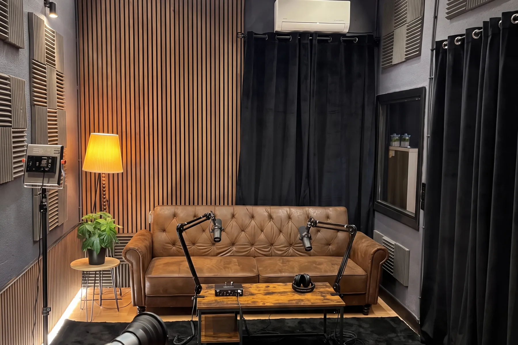 Estudio de grabación de Distrito Creativo: paneles acústicos, pared de listones de madera, sofá y dos micrófonos de podcast
