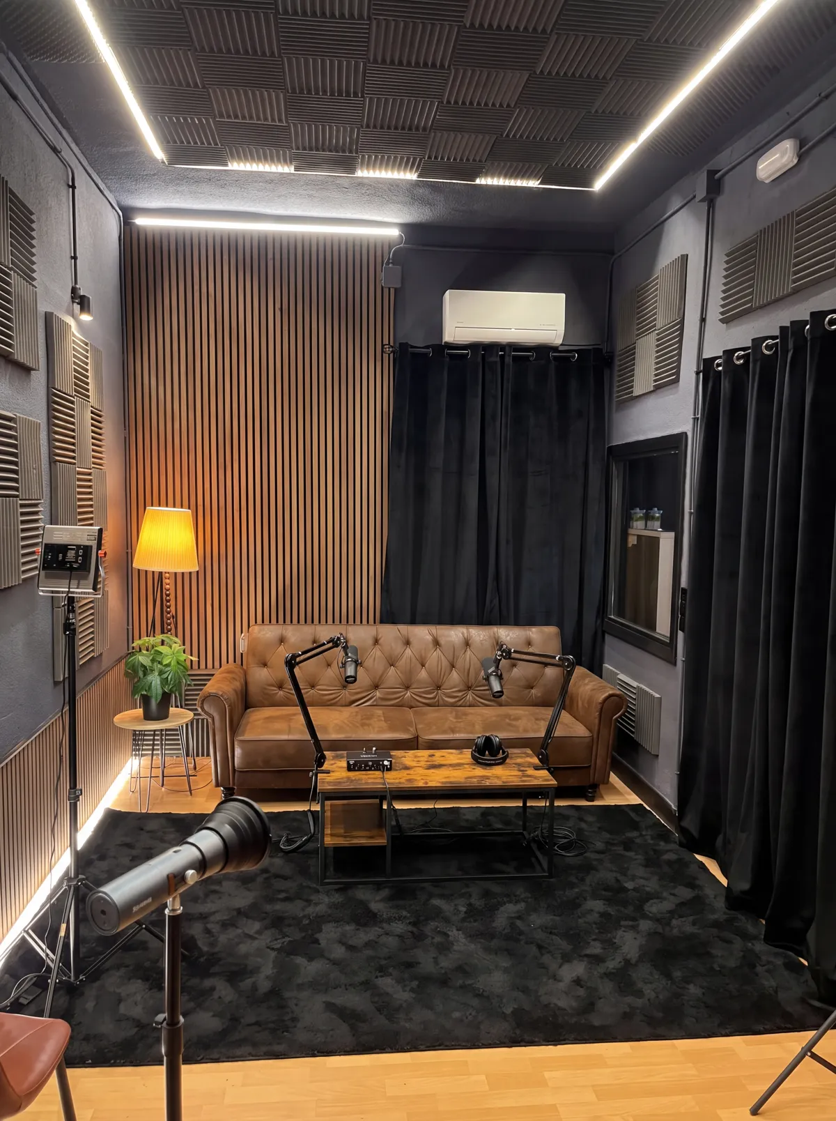 Estudio de grabación de Distrito Creativo: techo y paredes con tratamiento acústico, pared de listones, sofá, mesa y dos micrófonos de podcast